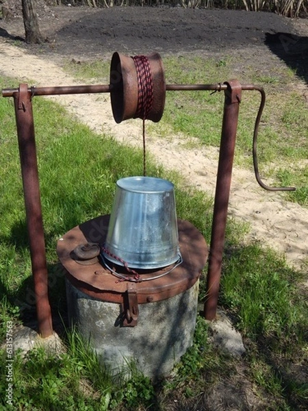 Obraz Rural well with clean water. A zinc bucket tied to a well of water.