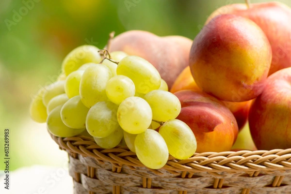 Fototapeta Fresh ripe apples, peaches, green and blue grapes in basket. Healthy food on table on defocus autumn background.