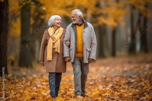 Fototapeta Happy senior man and woman walking on scattered yellowed leaves in scenic autumn park
