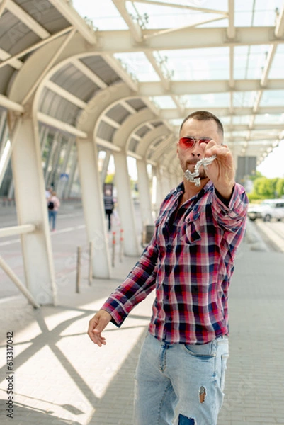 Fototapeta a handsome man nicely and stylishly dressed in pink glasses stands at a bus stop