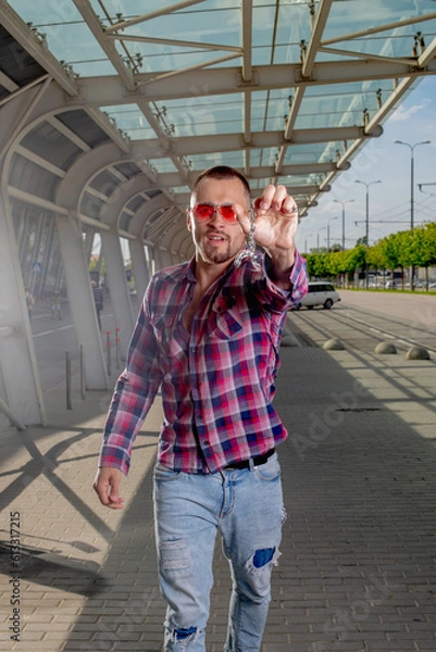 Fototapeta a handsome man nicely and stylishly dressed in pink glasses stands at a bus stop