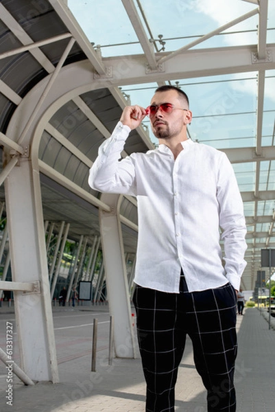 Fototapeta a handsome man nicely and stylishly dressed in pink glasses stands at a bus stop
