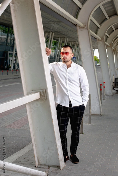 Fototapeta a handsome man nicely and stylishly dressed in pink glasses stands at a bus stop