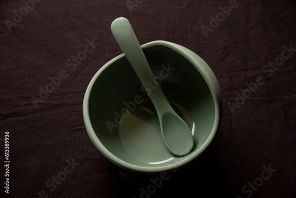 Fototapeta Empty dishes for baby, soft shatterproof tableware for the first feeding, spoon and bowl for baby food on black texture background.