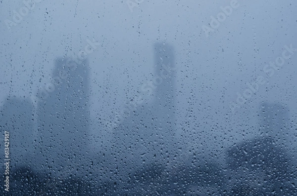 Fototapeta Rain drop on glass window in monsoon season with blurred city buildings background.