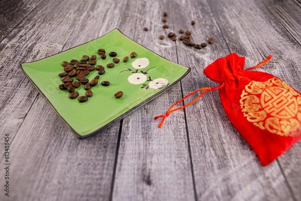 Fototapeta Coffee beans on a green saucer with a red pouch next to it, wooden background, photo at an angle