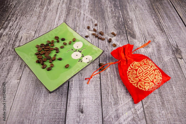 Fototapeta Coffee beans on a green saucer with a red pouch next to it, wooden background, photo at an angle