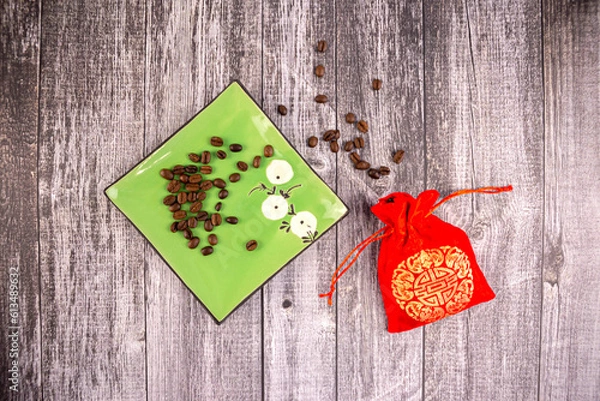 Fototapeta Coffee beans on a green saucer with a red bag next to it, wooden background, photo from above