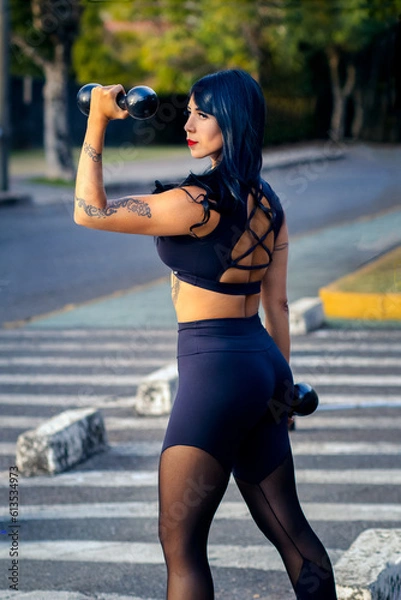 Obraz athlete woman exercising on the street with dumbbells and in gym clothes.