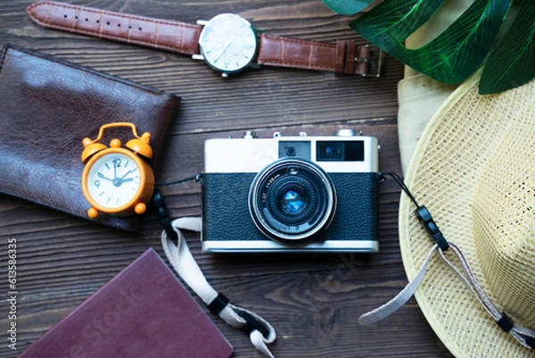 Fototapeta Top view of accessories for tourist to travel in Brown tone on Travel concept, Camera on notebook and airplane with passport and watch and hat with wallet  on wooden background.