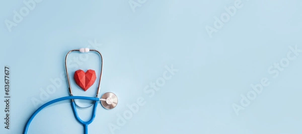 Fototapeta Blue stethoscope and red polydiagonal decorative heart on pastel background. Medical banner. Doctor's day concept. Selective focus, copy space