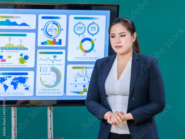 Fototapeta Millennial Asian professional successful female businesswoman lecturer presenter in formal business suit standing pointing computer monitor presenting graph chart financial info to businessman client