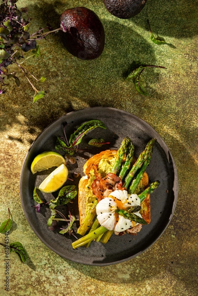 Fototapeta Grilled Toast witch Asparagus, avocado, Poached egg, greens, bacon on green textured background. banner, menu recipe place for text, top view. Traditional breakfast.