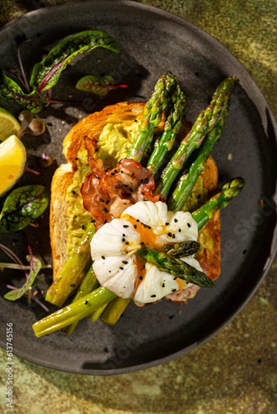 Fototapeta Grilled Toast witch Asparagus, avocado, Poached egg, greens, bacon on green textured background. banner, menu recipe place for text, top view. Traditional breakfast.