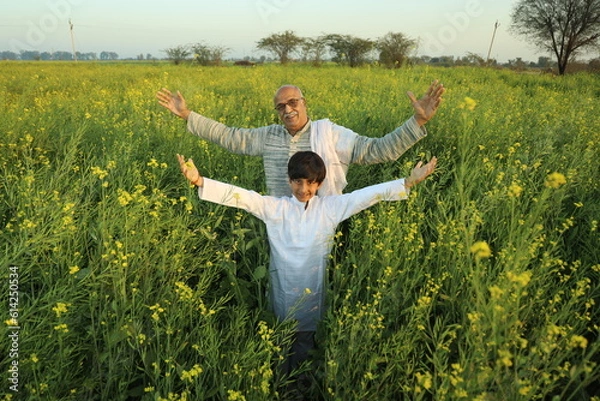 Obraz Happy Indian farmer standing in the mustard field with grand son and enjoying the benefits from the flourished rural mustard crop
