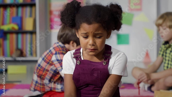 Fototapeta Close-up shot of upset African-American girl crying while playing with another kids in kindergarten