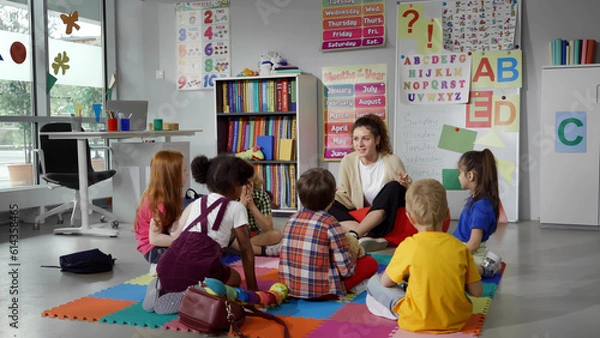 Fototapeta Small nursery school children with teacher sitting on floor having lesson
