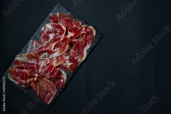 Obraz Tradition in every slice: the exquisiteness of acorn-fed Iberian ham on a black background.