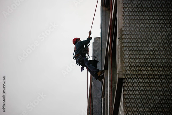 Obraz Window cleaning worker hanging on a building wearing safety equipement including harness and helmet.
