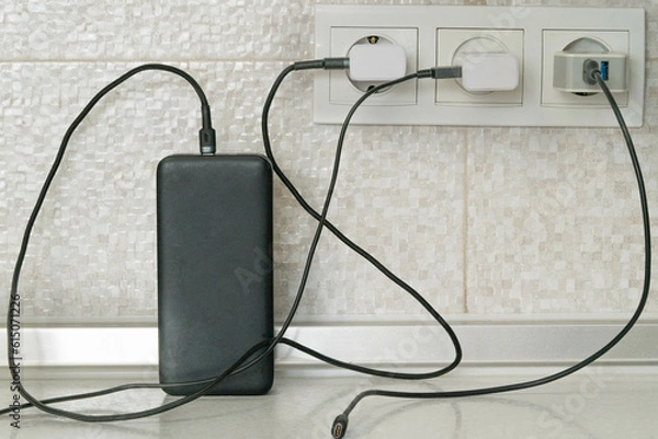 Obraz Three cables for charging electrical devices are plugged into electrical outlets, one of them charges the power bank
