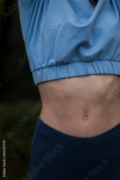 Fototapeta View of athletic body of a girl in blue gym suit in cloudy  weather.