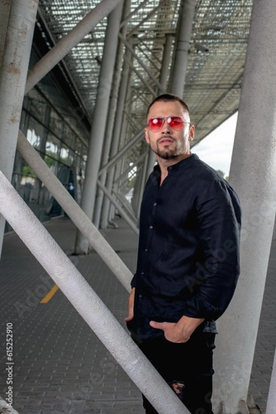 Fototapeta a stylish man in light pants and a black shirt against the background of empty walls holds glasses in his hands and looks away angrily