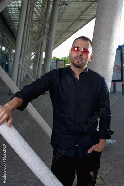 Fototapeta a stylish man in light pants and a black shirt against the background of empty walls holds glasses in his hands and looks away angrily