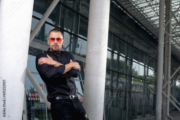 Fototapeta a stylish man in light pants and a black shirt against the background of empty walls holds glasses in his hands and looks away angrily
