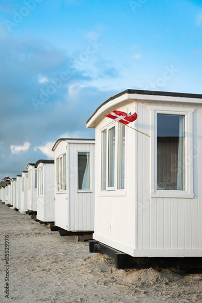 Fototapeta Blick von schräg vorne auf die Badehäuser am Strand von Løkken, an einem Haus hängt eine dänische Fahne, im Hintergrund ein Wohnhaus auf der Düne, vertikal 