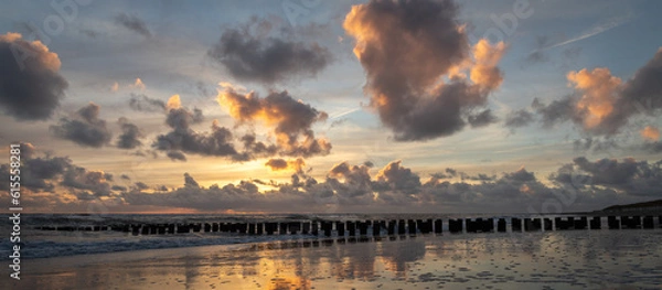 Fototapeta Sunset with colorful sky and clouds and wooden posts at Westenschouwen, Zeeland, the Netherlands