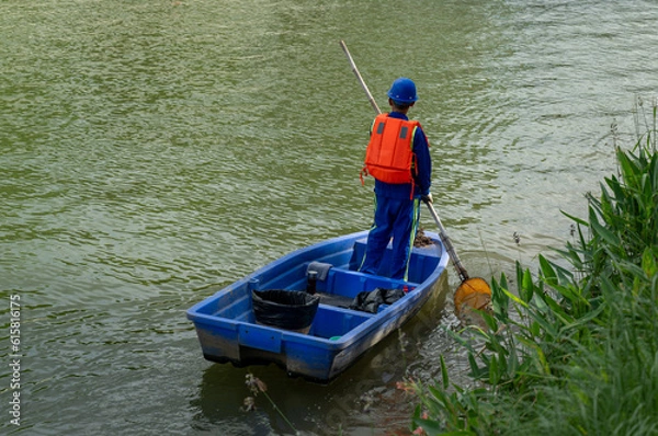 Fototapeta A worker stand in boat to collect garbage in river