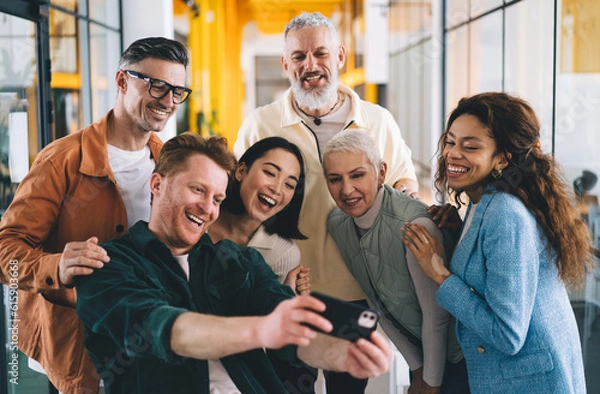 Fototapeta Group of smiling diverse people recording video on smartphone in office