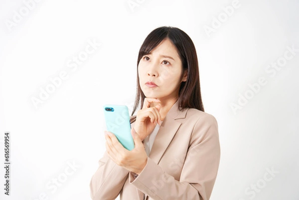 Fototapeta スマートフォンを持って考えるミドルエイジのビジネスウーマン　白背景
