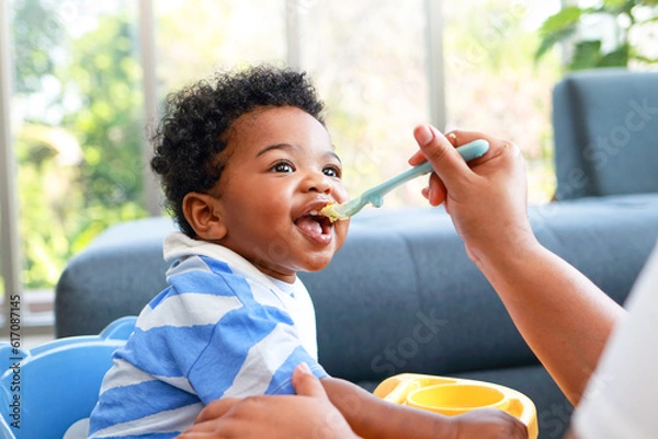 Fototapeta Happy smiling boy with mom while eating in the living room at home. Preschool child development, food menu for 1 year olds
