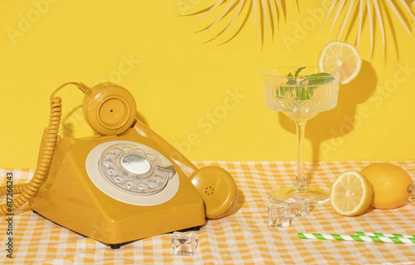 Fototapeta Summer creative layout with cocktail glass, lemons, drinking straws, ice cubes and yellow retro telephone with palm leaf on bright yellow and plaid background. 80s or 90s retro aesthetic 
