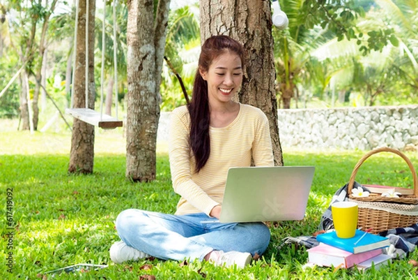 Fototapeta Asian student girl is studying  by laptop in nature with tree. Asian student is happy in study online and drinking coffee. Education in online life concept. Study Online in vacation.