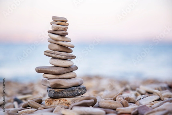 Fototapeta The pebble tower balances harmony stones on the Aegean sea beach at sunset. Relaxing peaceful spa tranquility concept with copy space for text 