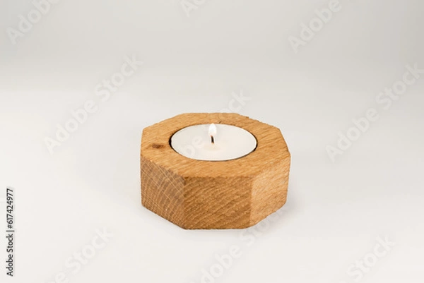 Fototapeta A lighted white wax candle burning in wooden stand isolated on white background with low light shadow.