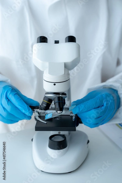 Fototapeta Doctor hand taking a blood sample tube from a rack with machines of analysis in the lab background, Technician holding blood tube test in the research laboratory.