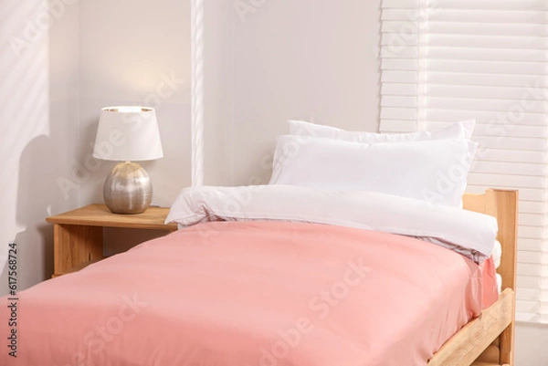 Obraz Comfortable bed with cushions and lamp on wooden bedside table in bedroom. Interior design