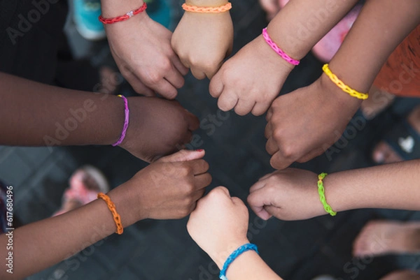 Fototapeta Multiethnic children hands together with rainbow bracelets. Friendship on a elementary age students group