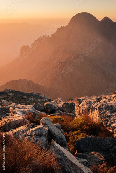 Obraz Dramatic mountain scenery and sunset haze with shining rocks and wild grasses in foreground.