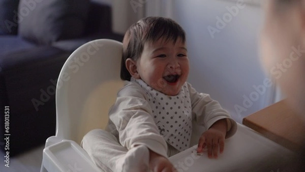 Obraz Back view of mom feeding her baby. Toddler is sitting on a high chair and eating with spoon
