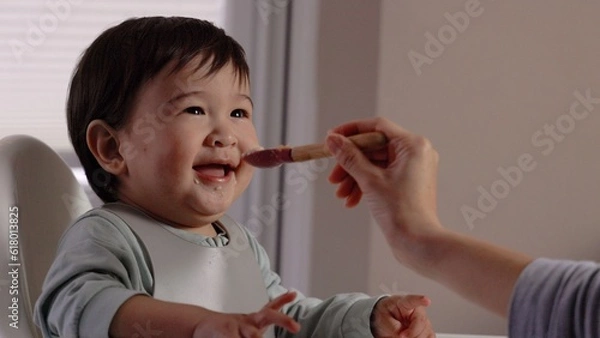 Obraz A happy baby smiling in the highchair and eating from the spoon