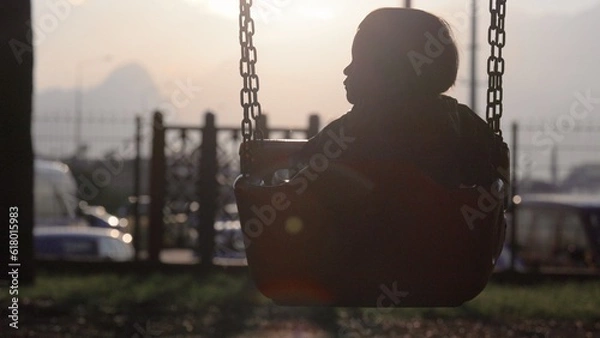 Obraz Silhouette of baby swinging on a swing towards the sun