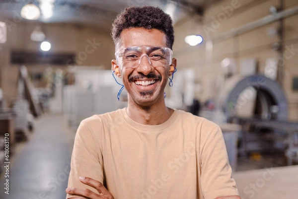 Fototapeta retrato de um homem afro Brasileiro professor de curso técnico de braços cruzados sorrindo para a câmera e usando óculo de proteção em um ambiente industrial