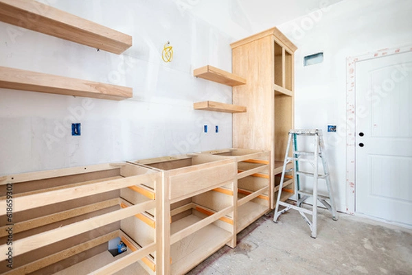 Fototapeta Built-in kitchen interior by the door, wooden cabinets and floating shelves installed at new building home. House renovation project at construction site, ready for drawers and countertops process.