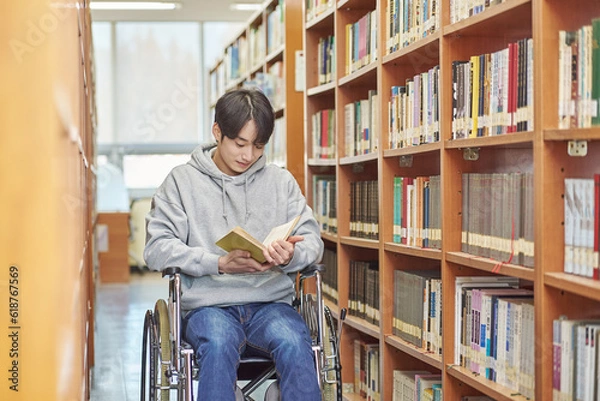 Fototapeta Asia South Korea university library bookcase in a wheelchair looking for a book on the shelf, physically handicapped young disabled male college student model