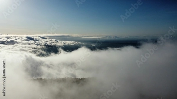 Fototapeta Stunning view of the clouds over the mountains covered in dense trees at sunlight