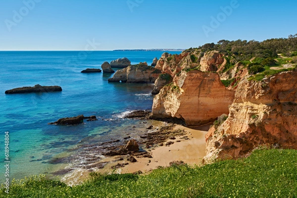 Fototapeta Solitary beach close to Alvor village in Portugal. There are lots of limestone rocks in the water and green grass in the foreground